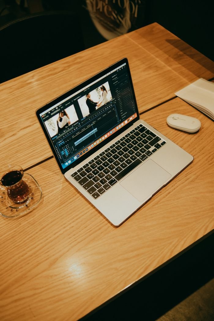 about-01 A laptop on a wooden table in a coffee shop, displaying video editing software for creative work.